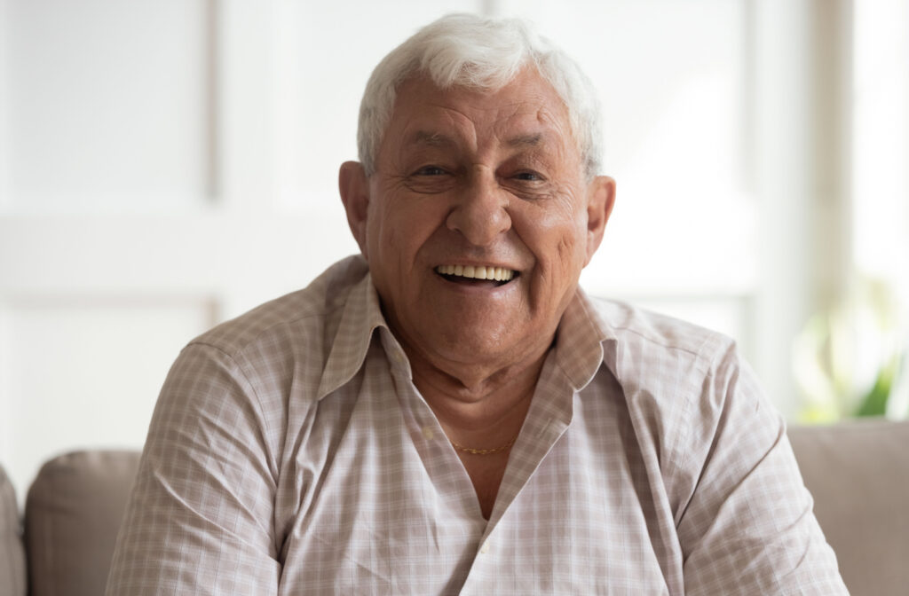A senior man sitting on the couch, smiling and looking directly at the camera