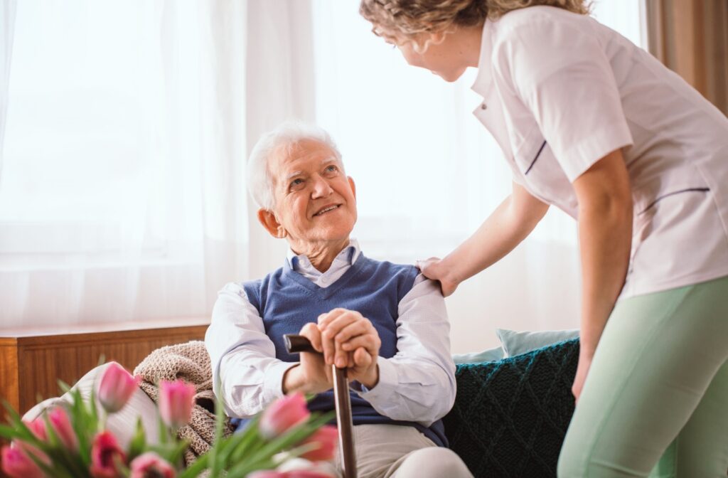 A caregiver at an assisted living community rests her hand on a resident's shoulder.