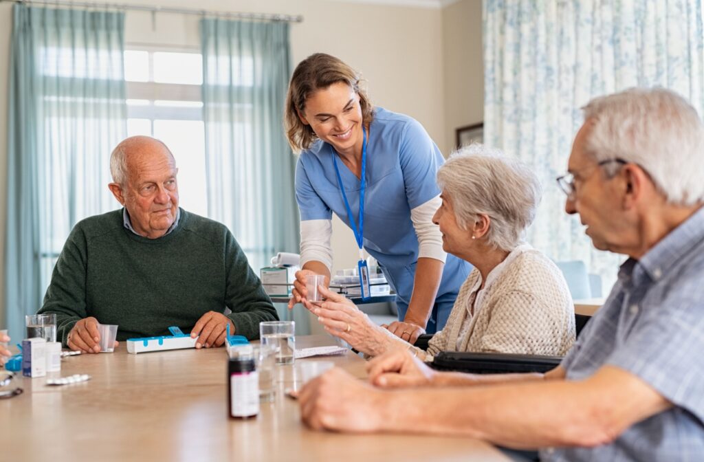 A caregiver helping three residents in assisted living manage their medication while smiling.